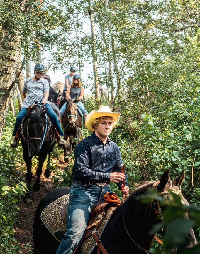 Thunder Ridge Trails Ranch_Guide takes group of people through forest on horse back